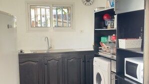 A compact kitchen with dark cabinets, a washing machine, a microwave, and a window with blinds.
