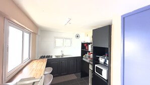 A compact kitchen with a gas stove, a microwave, and a sink. There is a window providing natural light and a clock on the wall. - At Misto, comfort and simplicity.  Open 24 hours a day Free Wi-Fi connection. (Ouangani)