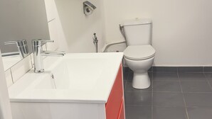 A modern bathroom with a white vanity, a green shelf unit, a toilet, and a tiled floor. - At Misto, comfort and simplicity.  Open 24 hours a day Free Wi-Fi connection. (Ouangani)