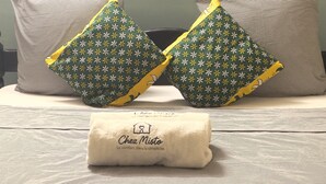A bed with striped bedding, two decorative pillows with a floral pattern, and a folded towel with text.