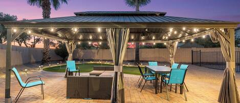 An outdoor patio with a covered seating area, a dining table, and chairs.