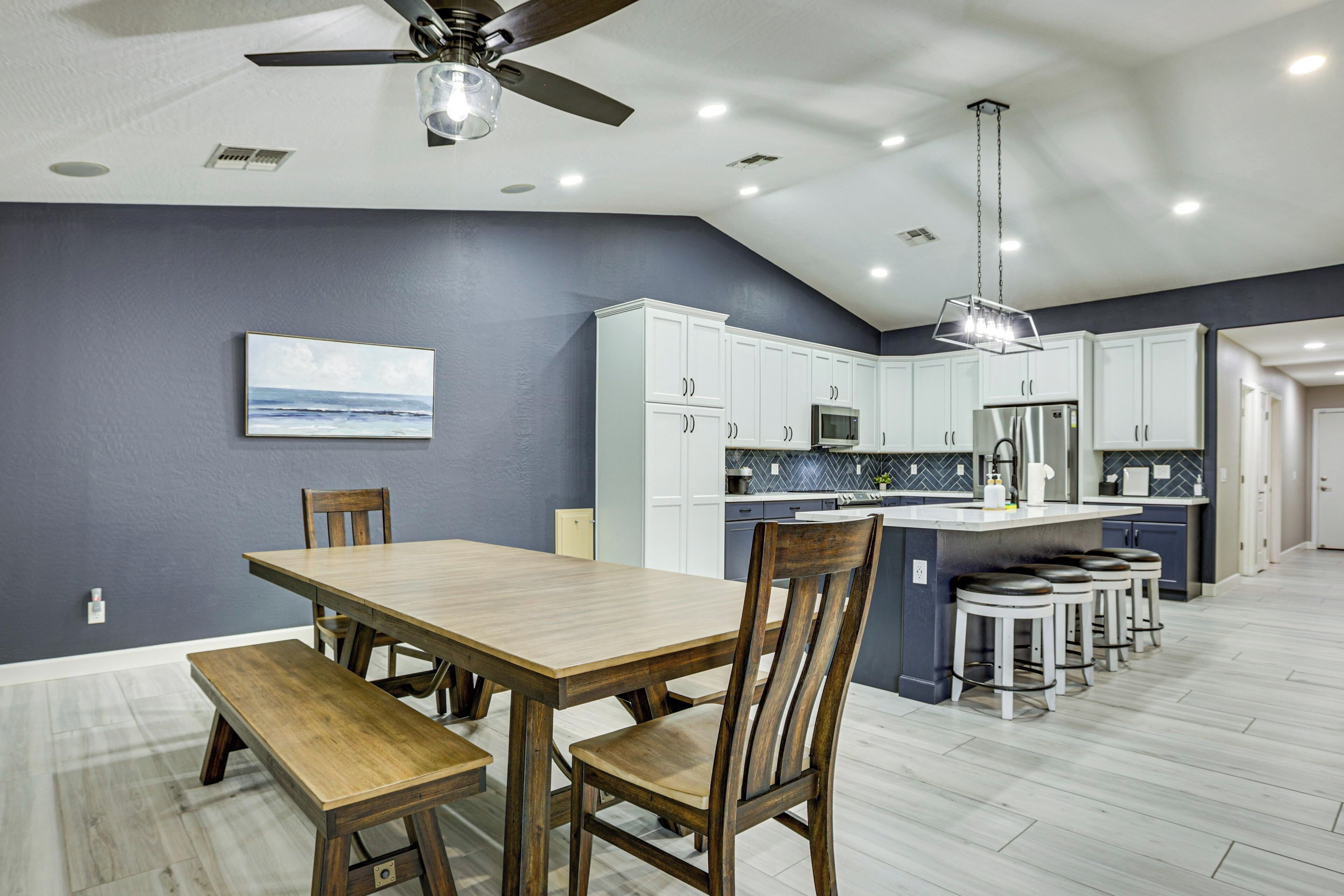 A modern kitchen with white cabinets, a central island with stools, a ceiling fan, and recessed lighting.