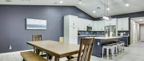 A modern kitchen with white cabinets, a central island with stools, a ceiling fan, and recessed lighting.