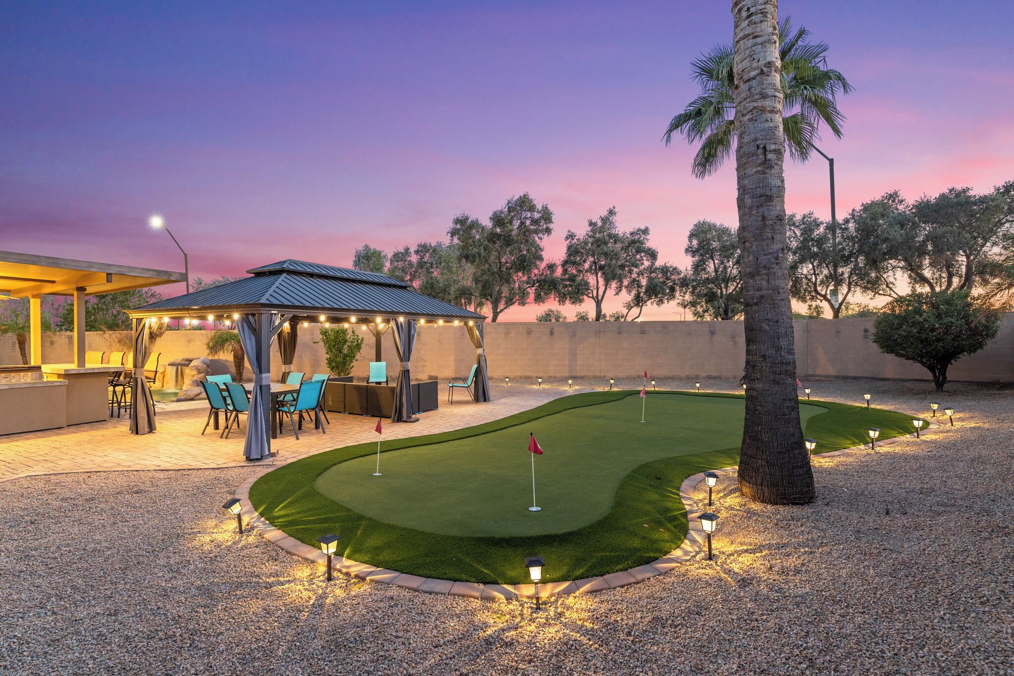 A well-lit outdoor area with a covered seating area, a putting green, and a palm tree.