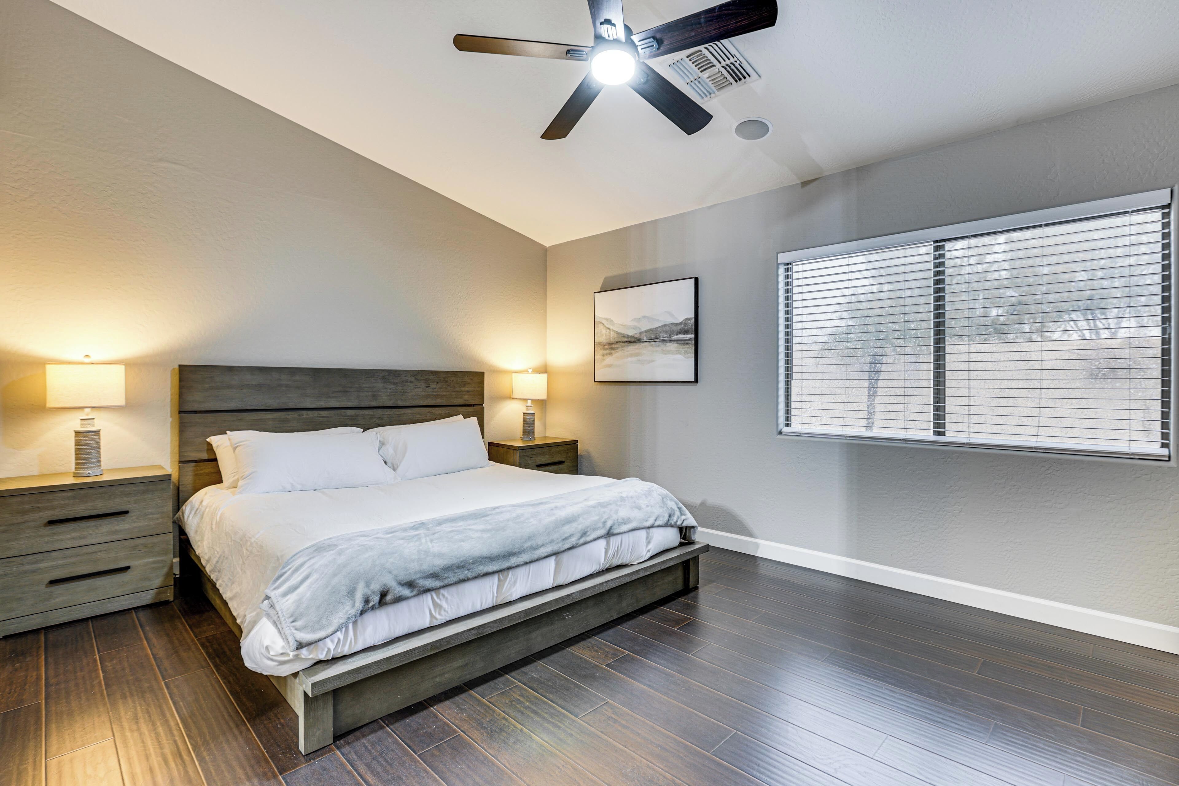 A bedroom with a bed, two bedside tables, a ceiling fan, and a window with blinds.