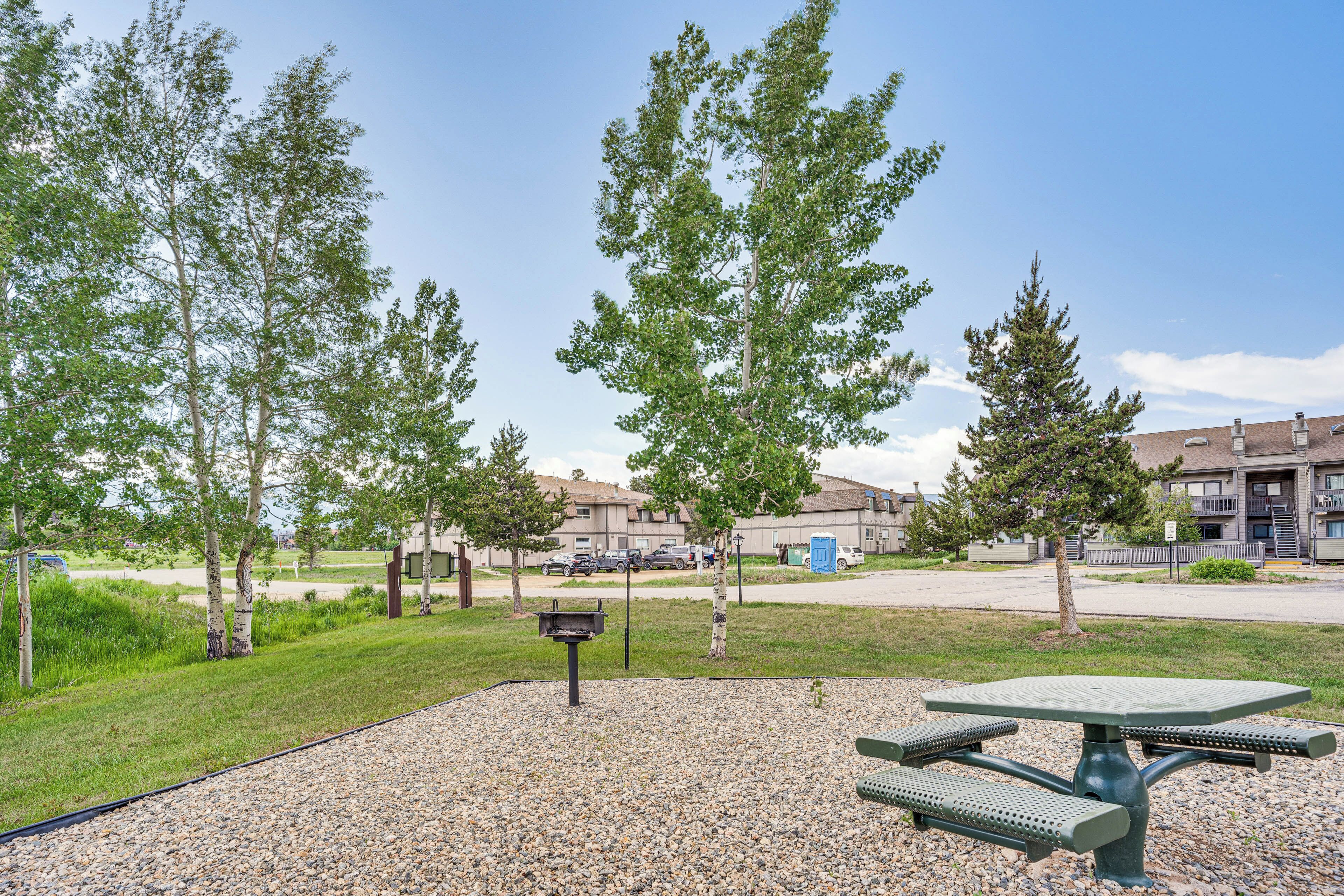 Un parc avec une table de pique-nique et des bancs, entouré d’arbres et d’une zone recouverte de gravier.