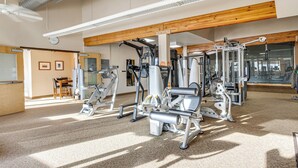 Une salle de sport équipée de divers appareils d’exercice, une horloge au mur et un plafond en bois.