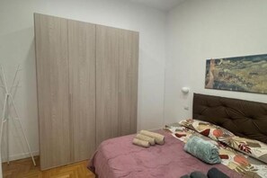 A bedroom with a bed, a wardrobe, a painting on the wall, and a tripod. - Casa Tecla - Your cozy retreat in the heart of Naples (Napoli)