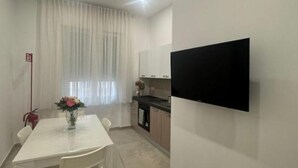 A modern kitchen with a flat-screen TV, a dining table with chairs, and a window with sheer curtains. - Casa Tecla - Your cozy retreat in the heart of Naples (Napoli)