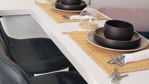 Een eettafel gedekt met zwarte kommen, wijnglazen en bestek, met een waterfles en een houten kist op de achtergrond.