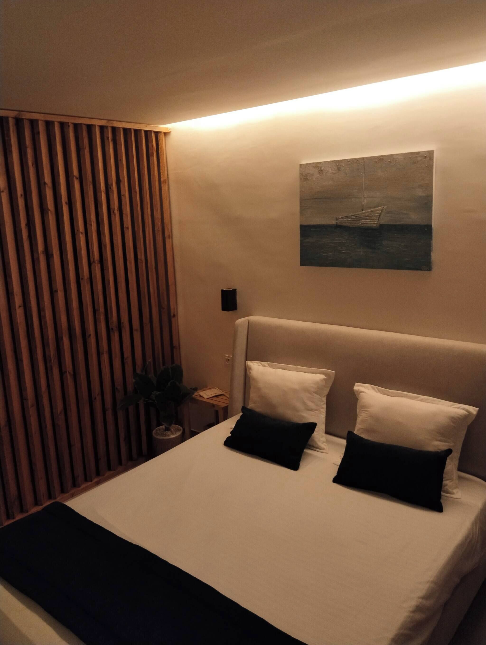 A neatly made bed with white and black pillows, a headboard, and a painting of a boat on the wall.