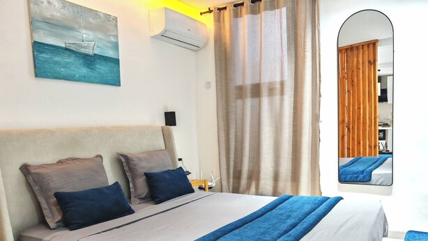Een net opgemaakt bed met een blauwe deken, een schilderij van een boot aan de muur, en een spiegel die een kamer met een bed weerspiegelt.