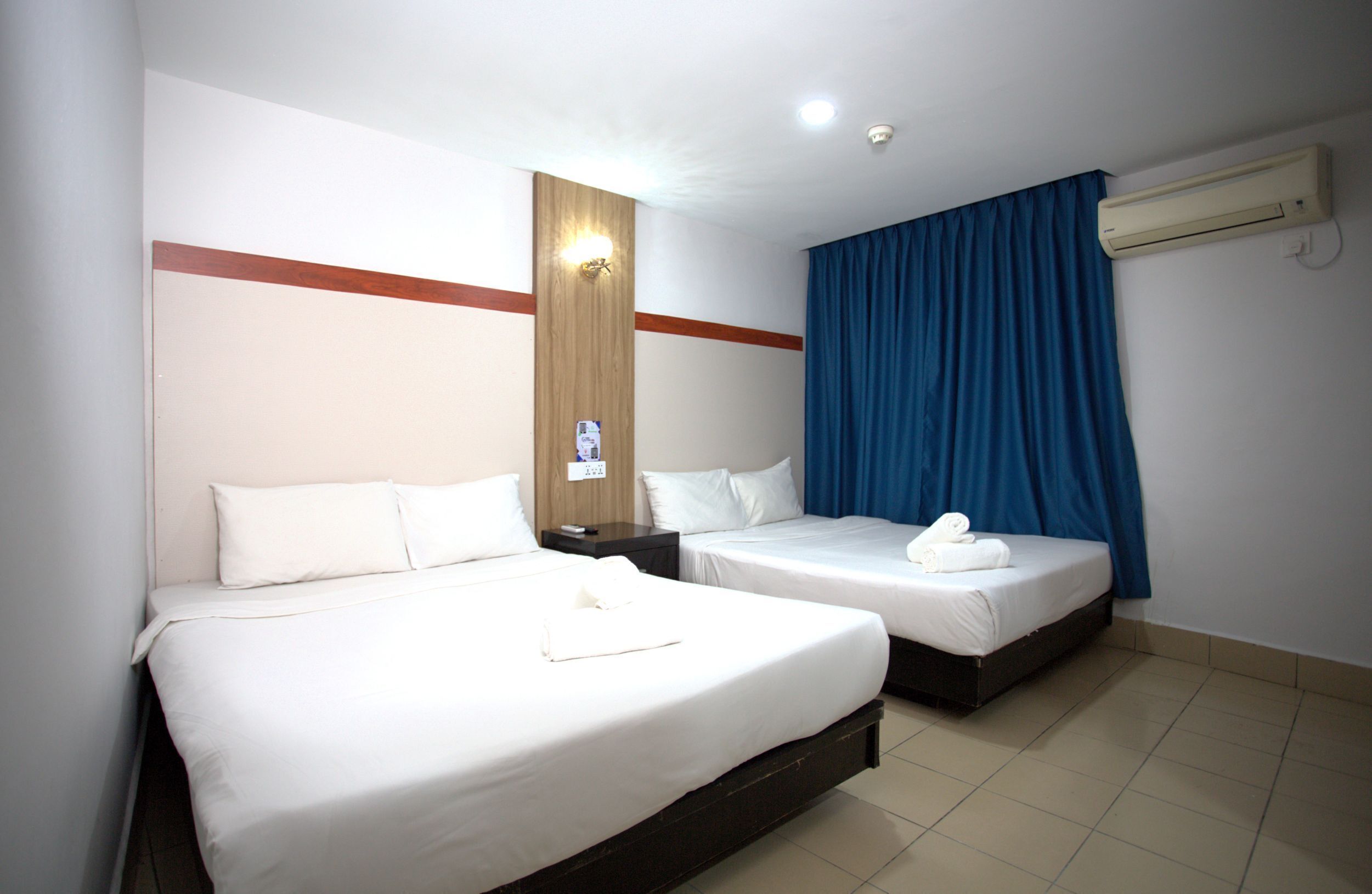 Une chambre d’hôtel avec deux lits simples, un mur décoratif en bois, un rideau bleu et un appareil de climatisation.