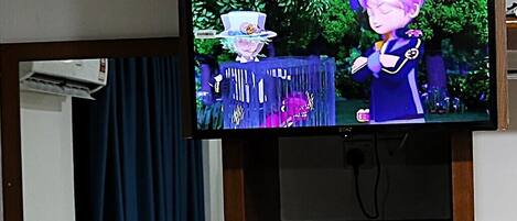 Un televisor montado sobre un soporte de madera con un estante inferior que muestra botellas de agua y una tetera.