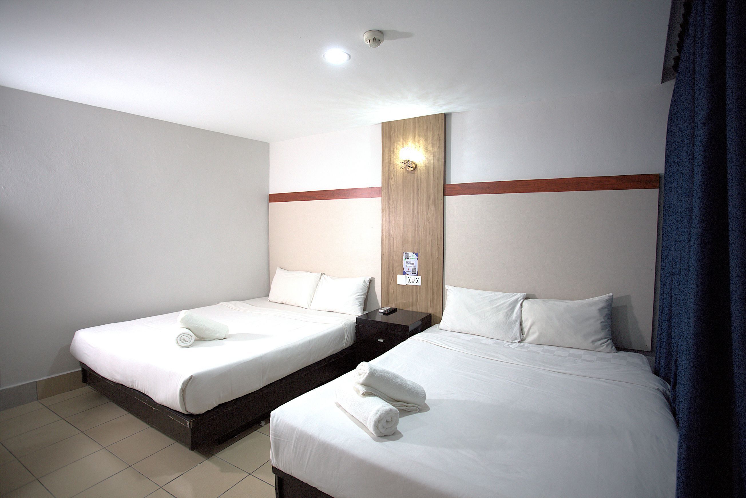 A hotel room with two single beds, a wooden headboard, a wall-mounted light, and a small table with a remote control.