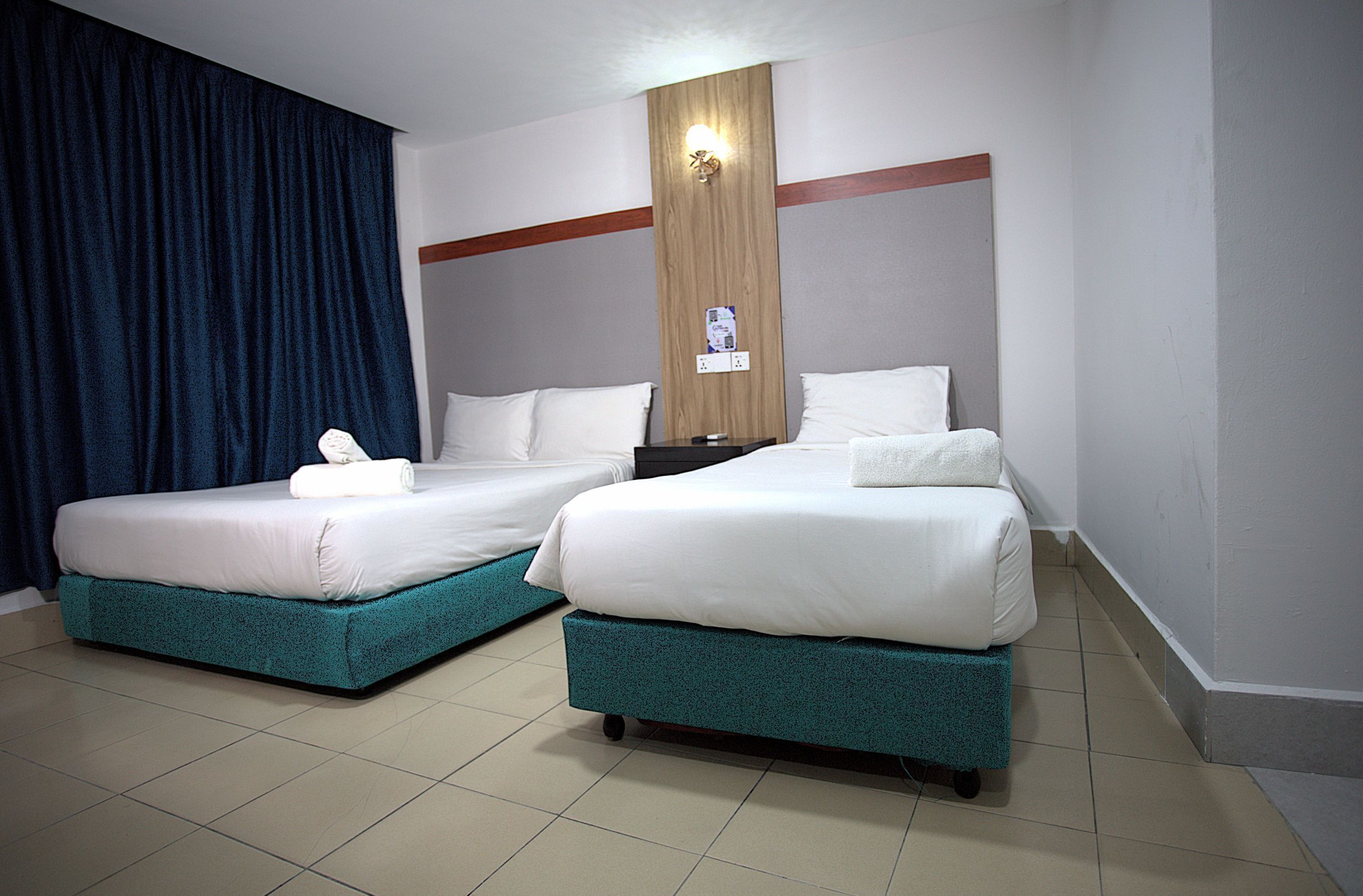 Una habitación de hotel con dos camas, un cabecero de madera y una cortina azul.