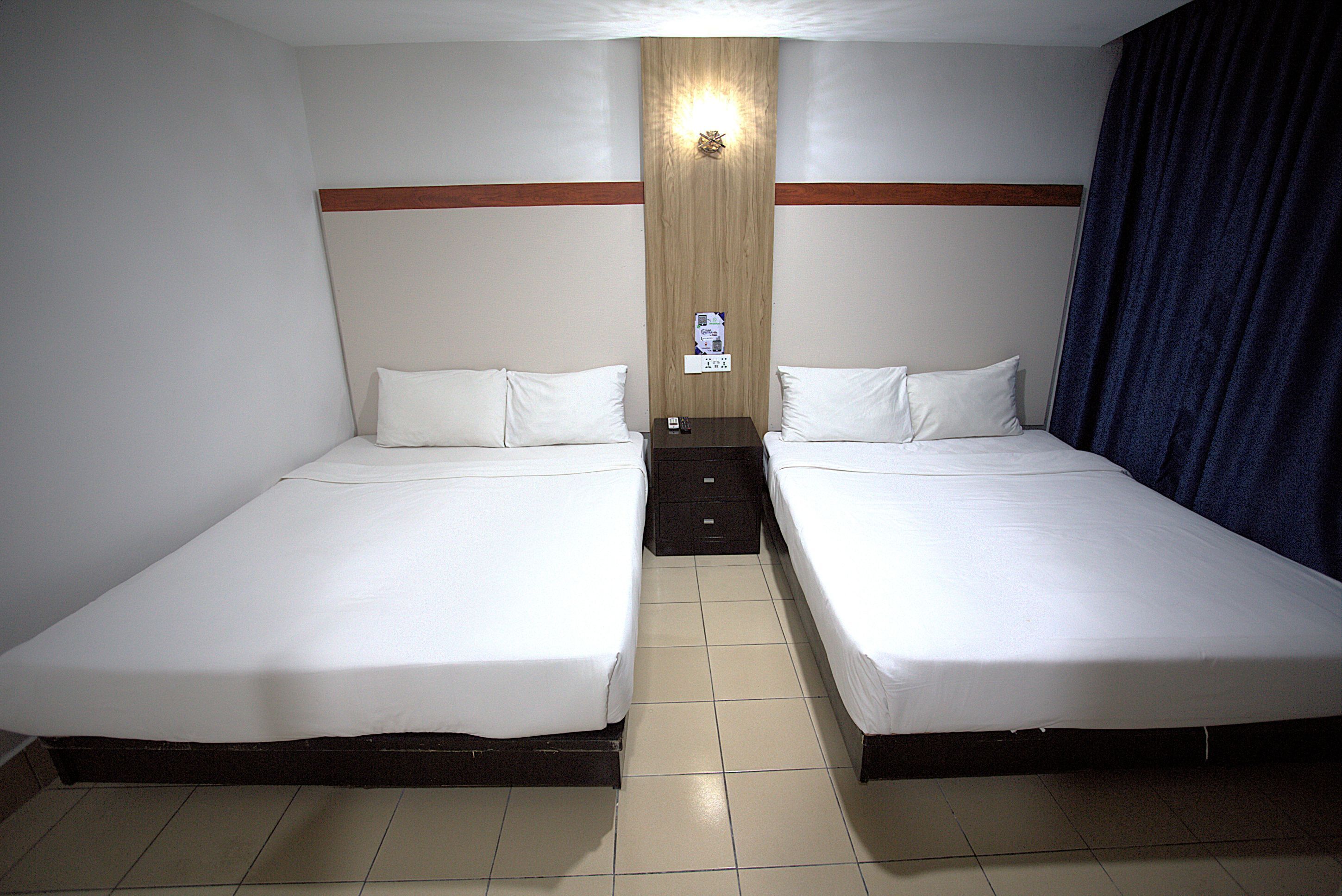 A hotel room with two single beds, a wooden headboard, a nightstand, and a wall-mounted light.