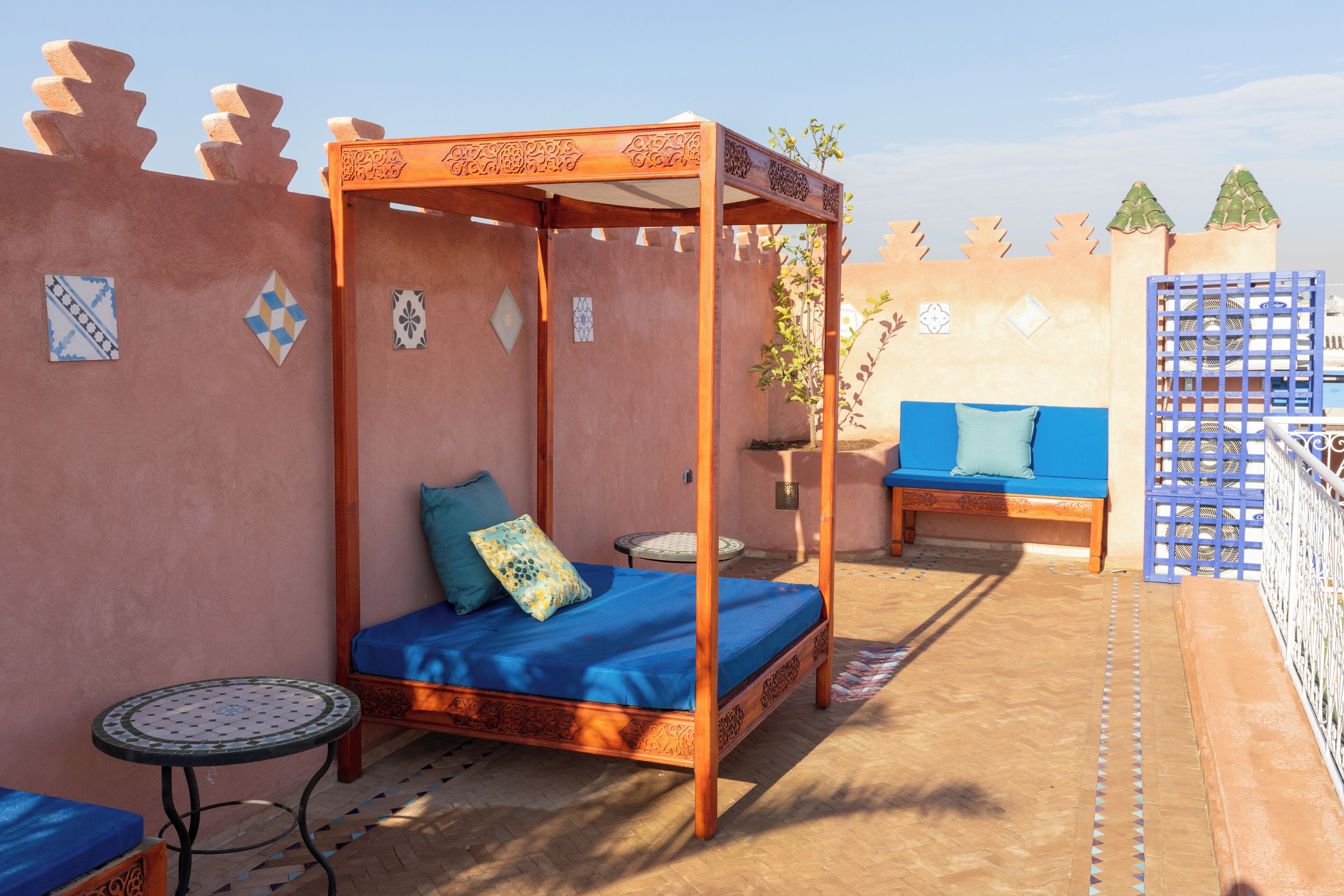 A four-poster bed with a blue mattress and a single pillow, a small round table with a blue cushion, and a blue sofa with a cushion.