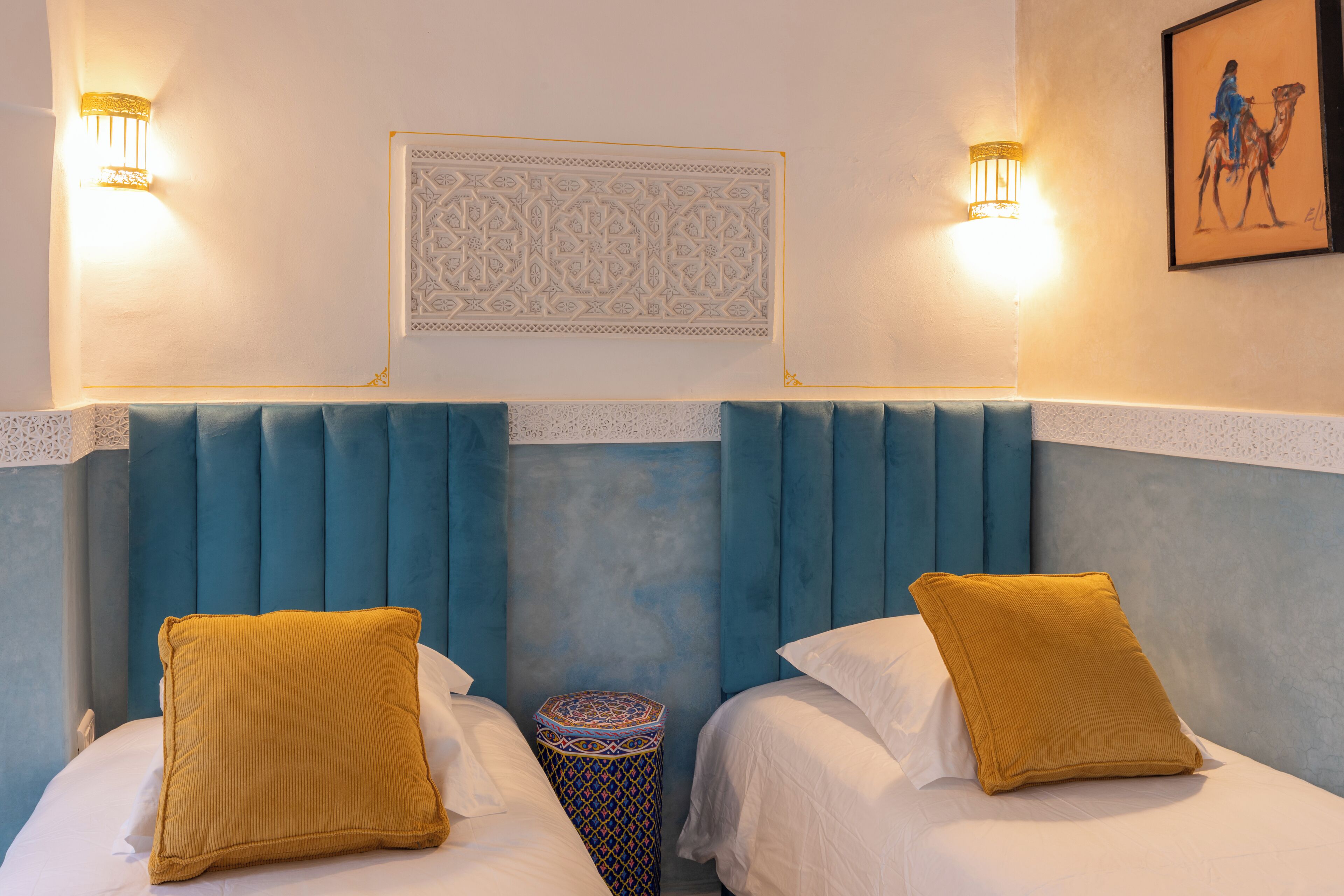 Hotelkamer met twee bedden, elk met een geel kussen, een decoratief paneel en twee wandlampen.
