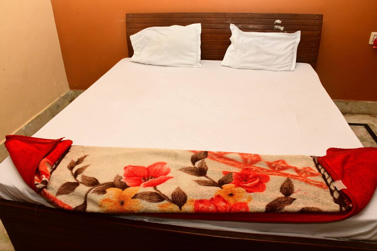 A bed with white sheets and two white pillows, a floral blanket, and red pillows on either side.