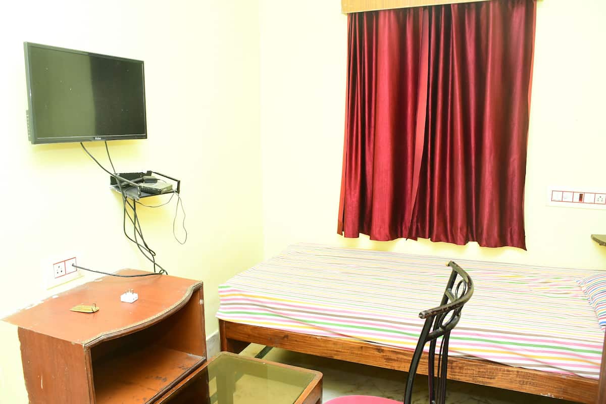 A room with a bed, a desk, a television mounted on the wall, and a window with a red curtain.