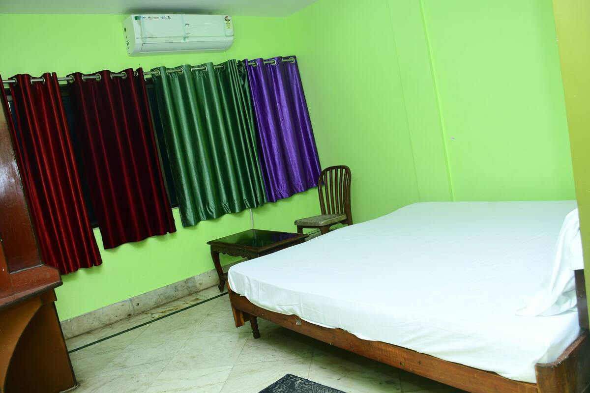 A room with a bed, a chair, a small table, and curtains in various colors.