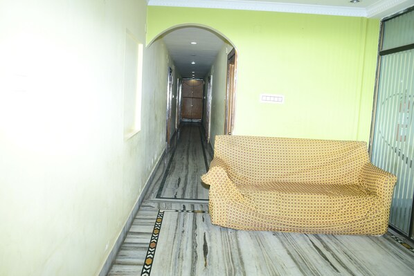 A hallway with a patterned sofa, a marble floor, and a door at the end. - Hotel Sampark (Bhadrak)