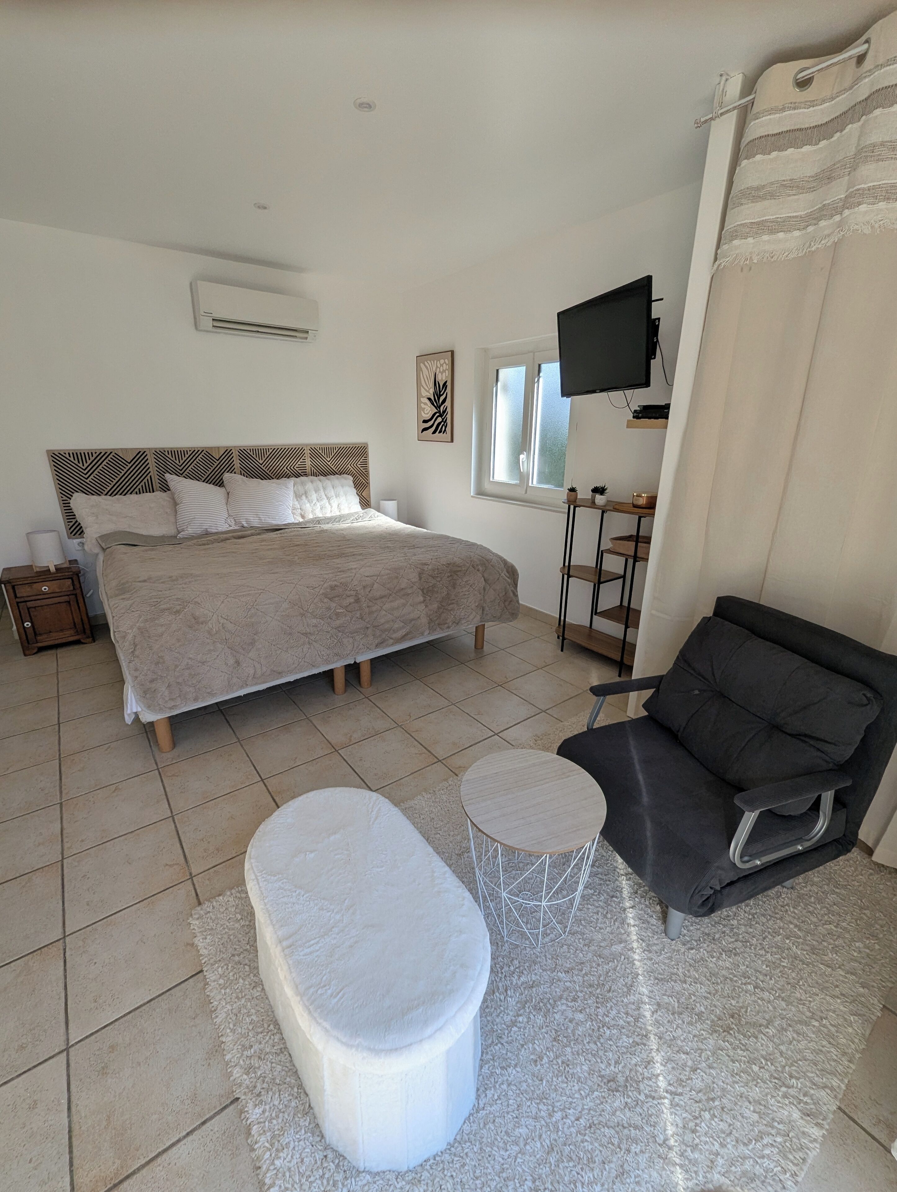 A bedroom with a bed, a sofa, a small round table, a TV, and a window.