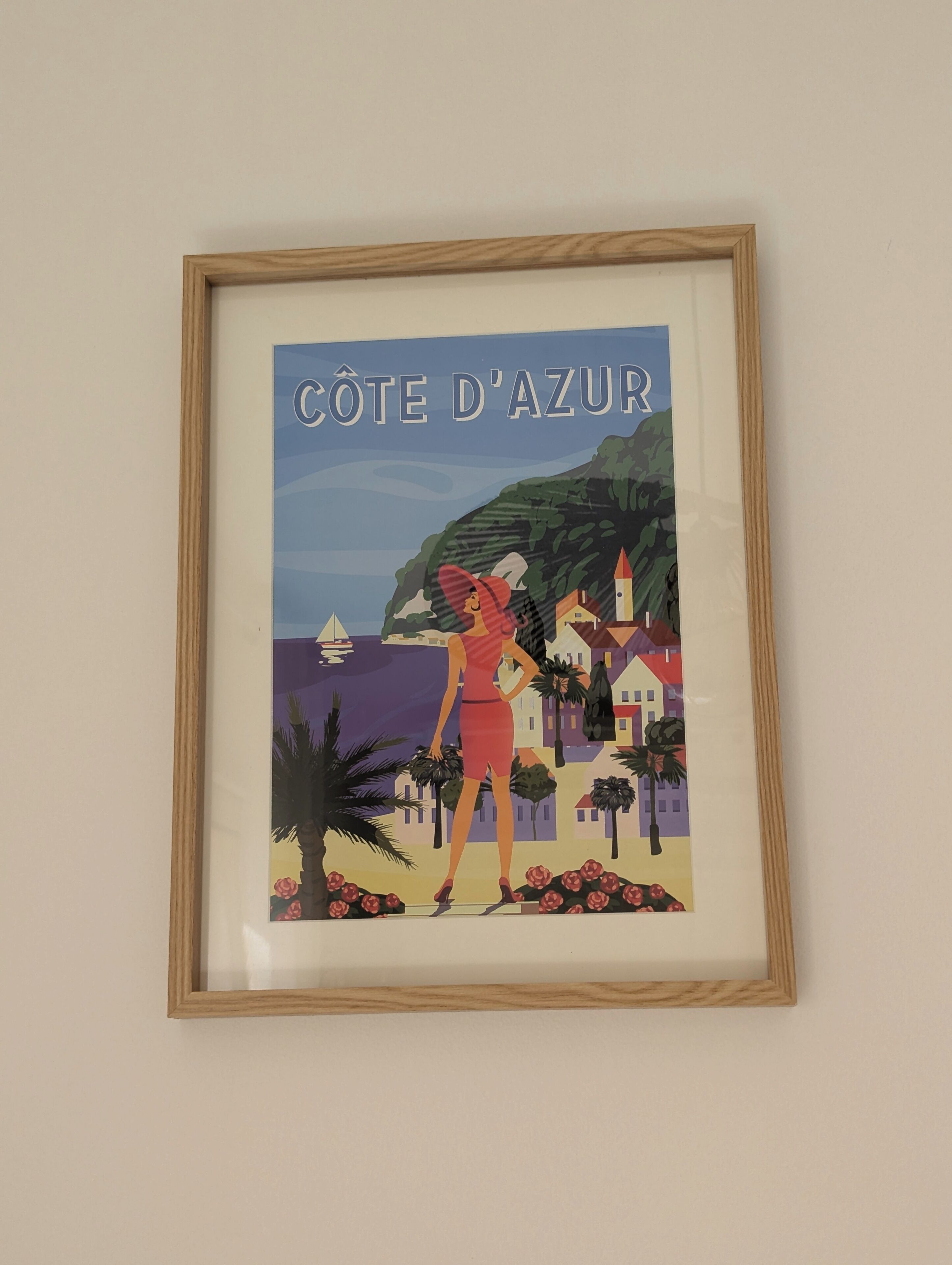 Ein gerahmter Posterabdruck der Côte d'Azur mit einer Frau, Palmen und Gebäuden.
