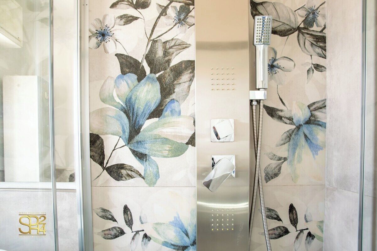 Un baño con arte floral en las paredes, ducha con cabezal de ducha de mano y mampara de vidrio.