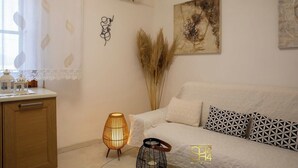 Ein modernes Wohnzimmer mit einem weißen Sofa, gemusterten Kissen, einer Wanddekoration und einem kleinen Tisch mit einer Laterne.