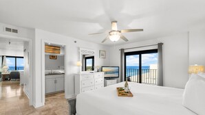 Une chambre d’hôtel avec un grand lit, un ventilateur de plafond, une télévision, un balcon avec vue sur la mer et un bureau avec une chaise.