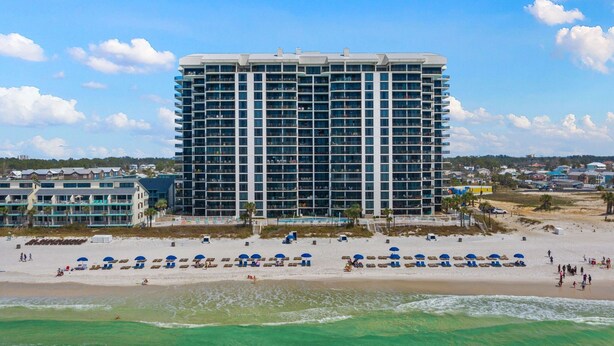 Un hôtel de grande hauteur doté de nombreux balcons, une plage avec des chaises longues et une vue dégagée sur l’océan.