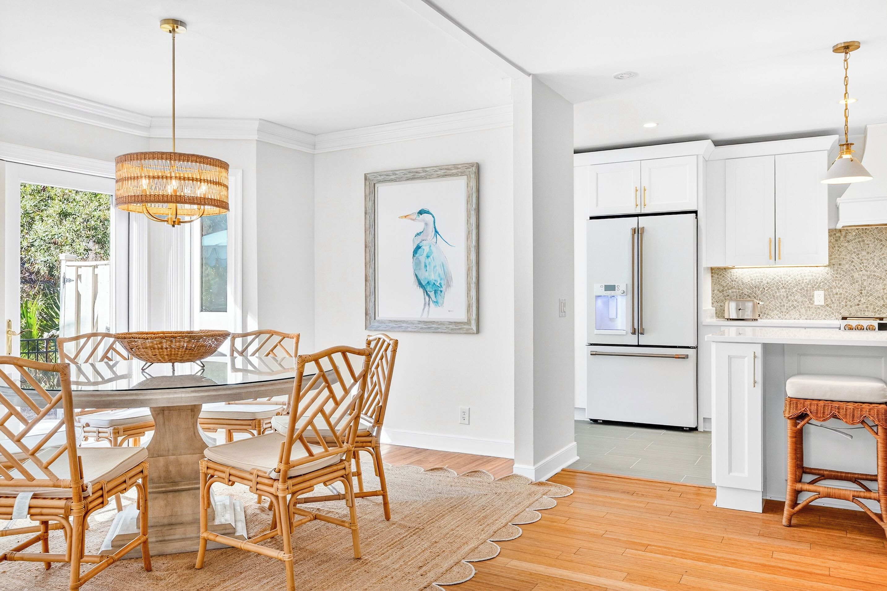 Una cocina moderna con armarios blancos, un refrigerador de acero inoxidable y un comedor con sillas de mimbre y una mesa de vidrio.