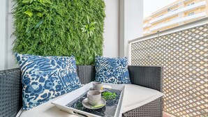 A balcony with a wicker sofa, patterned cushions, a tray with a cup and saucer, and a green vertical garden wall. - Sunny Apartment with Shared Pool (Portimão)