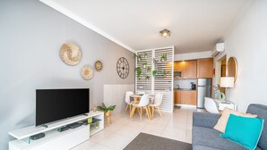 A modern living room with a flat-screen TV, a grey sofa, a dining area, and a kitchen in the background. - Sunny Apartment with Shared Pool (Portimão)