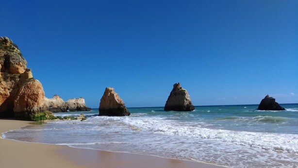 A beach with clear blue sky, sandy shore, and large rock formations. - Sunny Apartment with Shared Pool (Portimão)