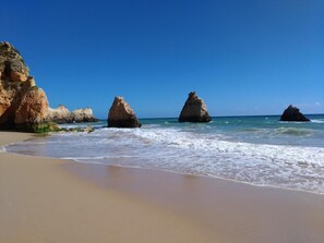 Una spiaggia con cielo azzurro, litorale sabbioso e ampie formazioni rocciose.