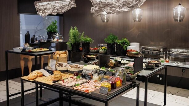 A buffet setup with various food items and plants, with a modern interior design and hanging light fixtures. - Hotel 3Trio (Bialystok)
