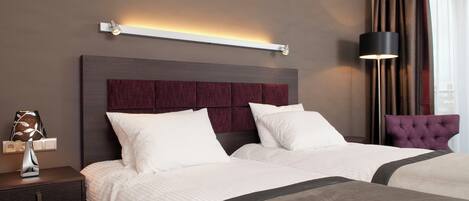 A hotel room with a large bed, a nightstand, a lamp, and a view of the city through the window.