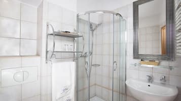 Un baño moderno con ducha de vidrio, un lavabo blanco y un espejo con marco decorativo.
