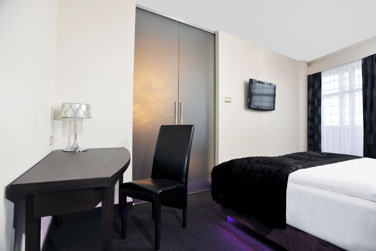Una habitación de hotel con una cama, un escritorio con una silla, un televisor y un armario.