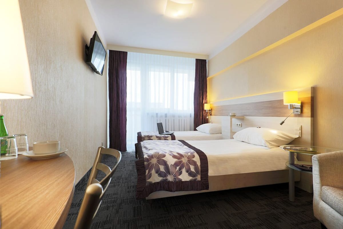 Habitación de hotel con cama, mesitas de noche, televisión, escritorio con silla y ventana con cortinas.