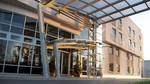 A modern building with a glass entrance, a covered outdoor area, and a multi-story structure with balconies. - Hotel 3Trio (Bialystok)