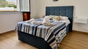Een net opgemaakt bed met gestreepte lakens, een blauw hoofdbord en een decoratief object aan de muur.