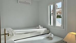 Een eenpersoonskamer met een raam, een wandairconditioner en een bedlampje.