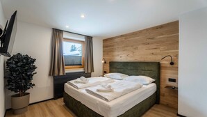 Ein modernes Hotelzimmer mit einem großen Bett, einem wandmontierten Flachbildfernseher, einer Topfpflanze und einem mit Vorhängen versehenen Fenster.