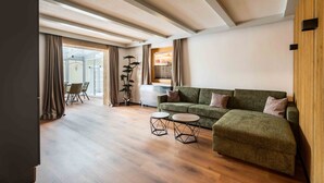 Ein modernes Wohnzimmer mit einem grünen Sofa, zwei runden Couchtischen, Holzböden und einem großen Fenster mit Vorhängen.