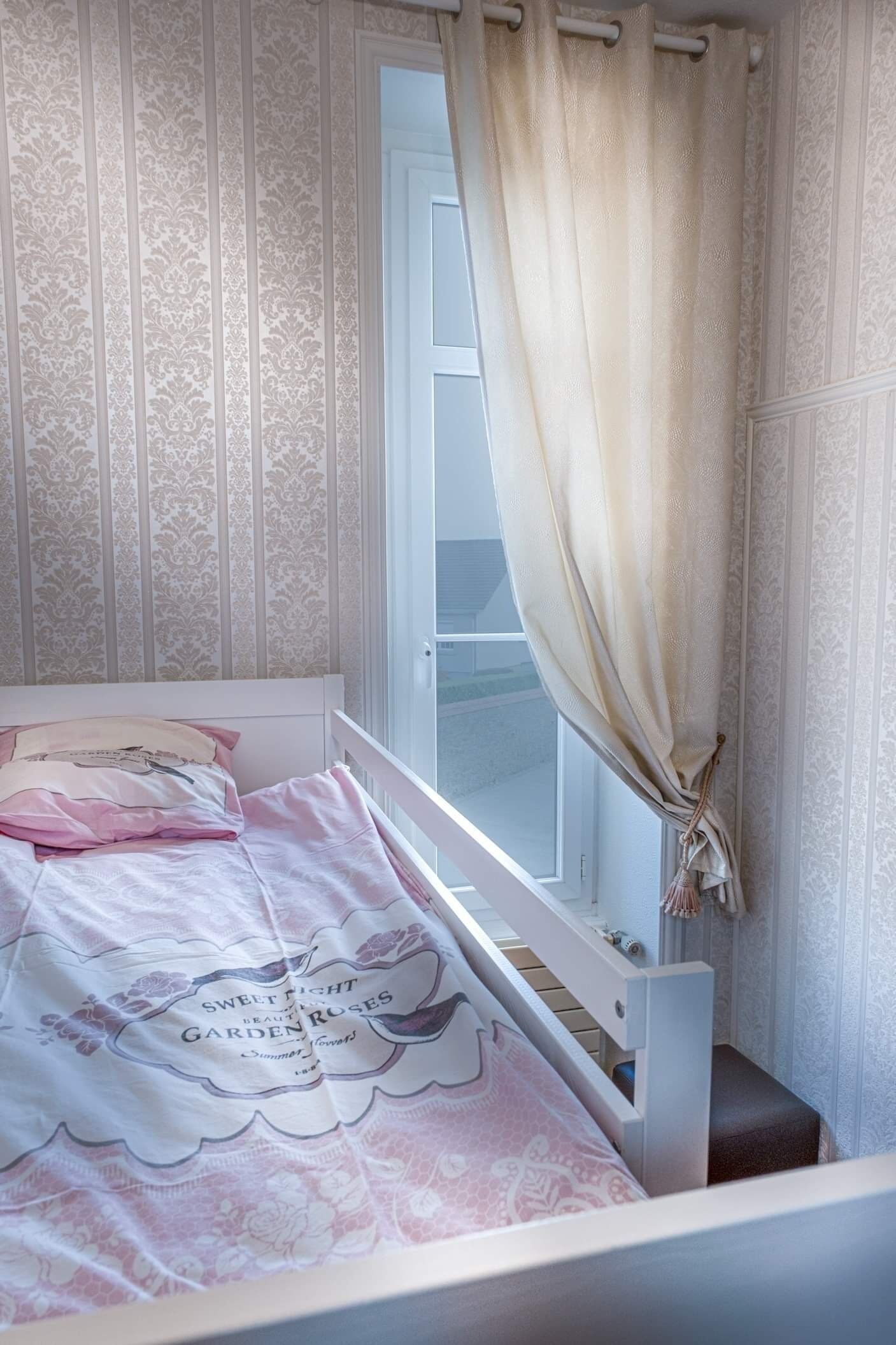 Une chambre à coucher avec un lit, une fenêtre avec des rideaux et un papier peint à motifs.