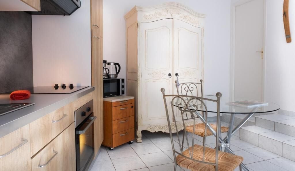 Een kleine keuken met een magnetron, oven en een kast. Er is een eettafel met stoelen en een klein glazen bijzettafeltje.